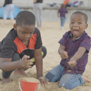 Two young boys are playing on the sand on their family holiday.